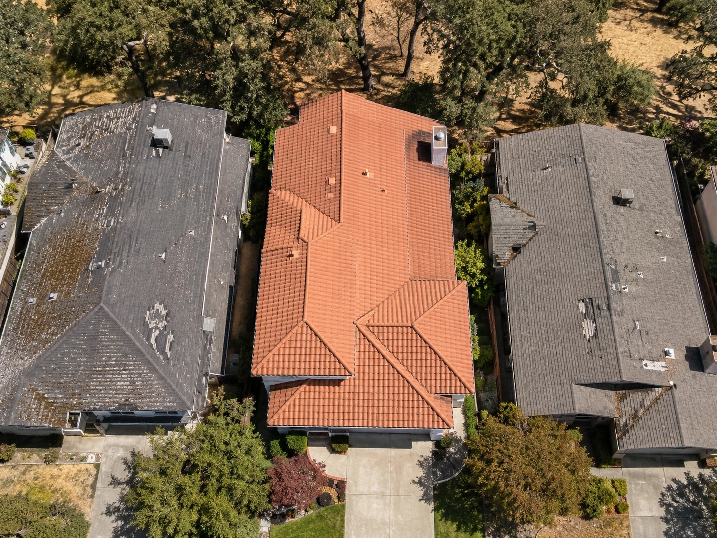 Aerial view of three residential roofs, with a clay tile roof in the center flanked by two asphalt shingle roofs